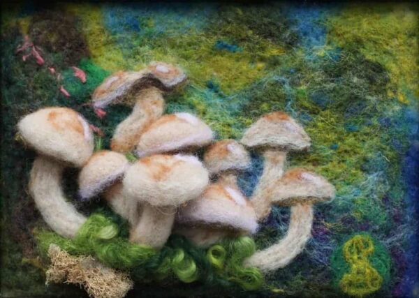 A cluster of small brown mushrooms crafted from needle felted wool some 2d and some 3d sit in front of a dark brown and vibrant cerulean blue and green background